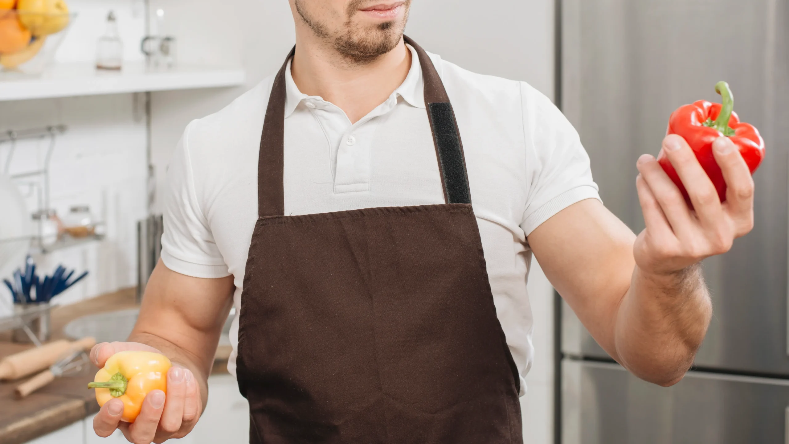 Man wearing leather cooking apron while holding bell peppers